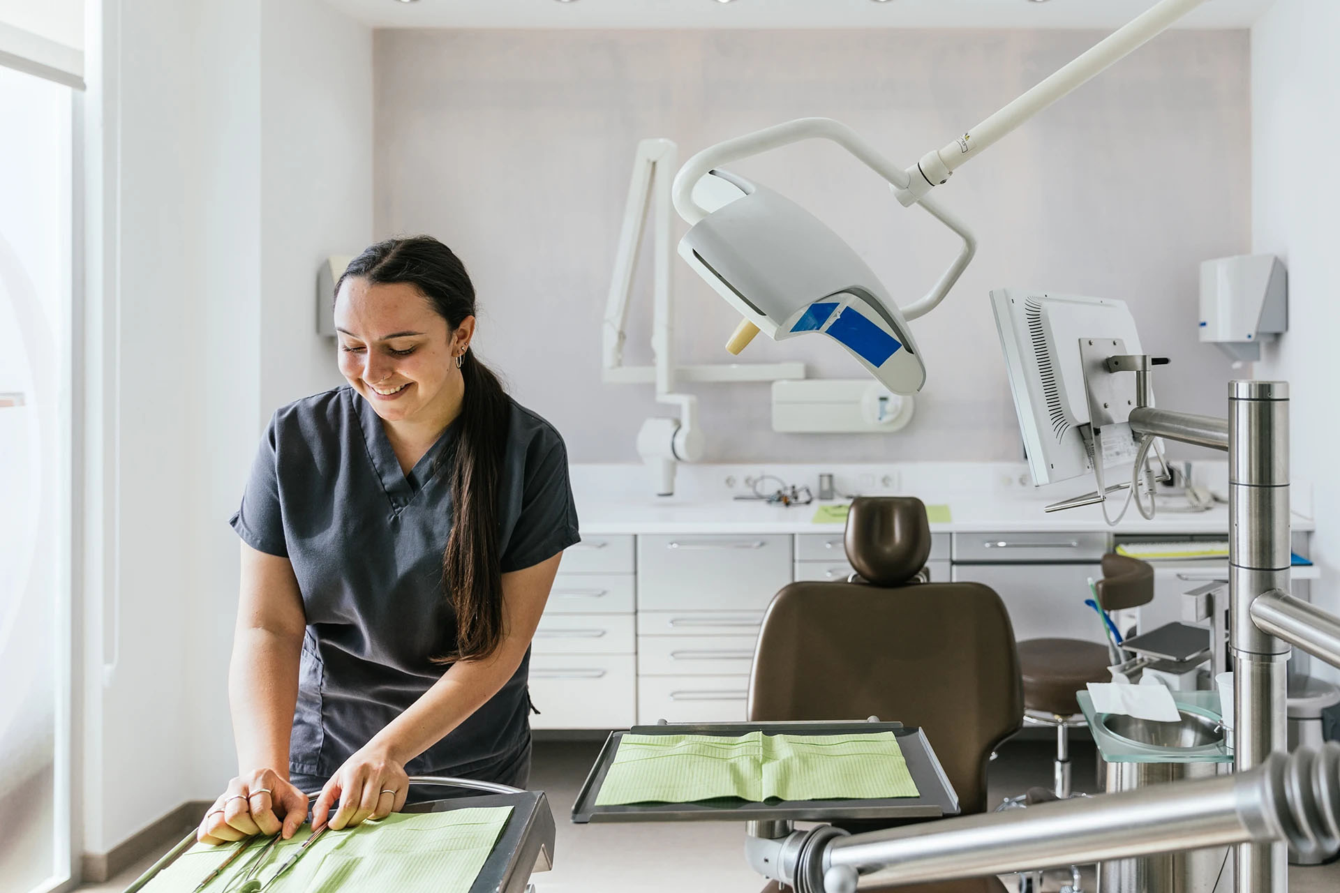 Smiling dental assistant in gray scrubs arranging instruments on a tray in the treatment room