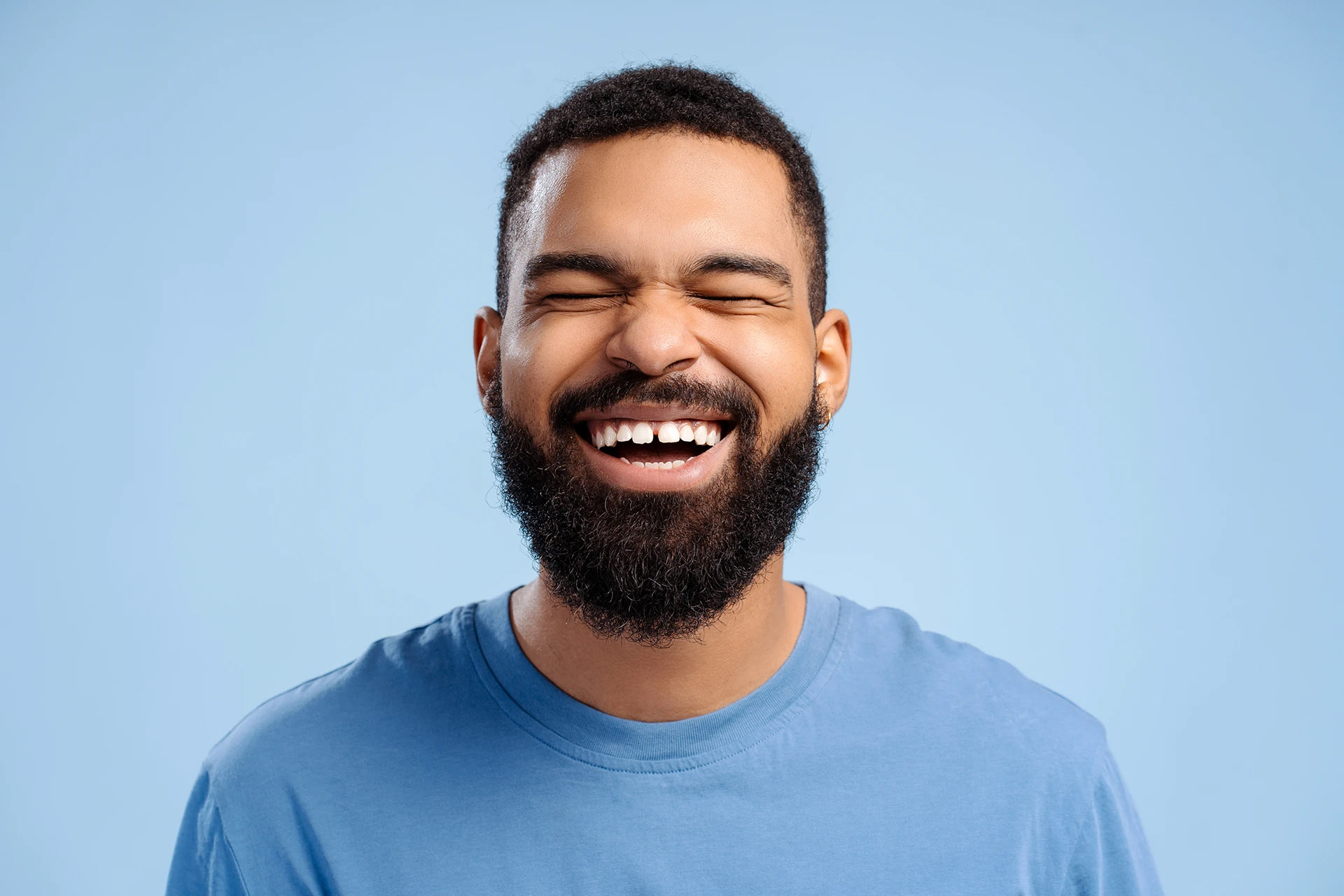 Studio portrait of a bearded man in a blue shirt laughing against a blue background