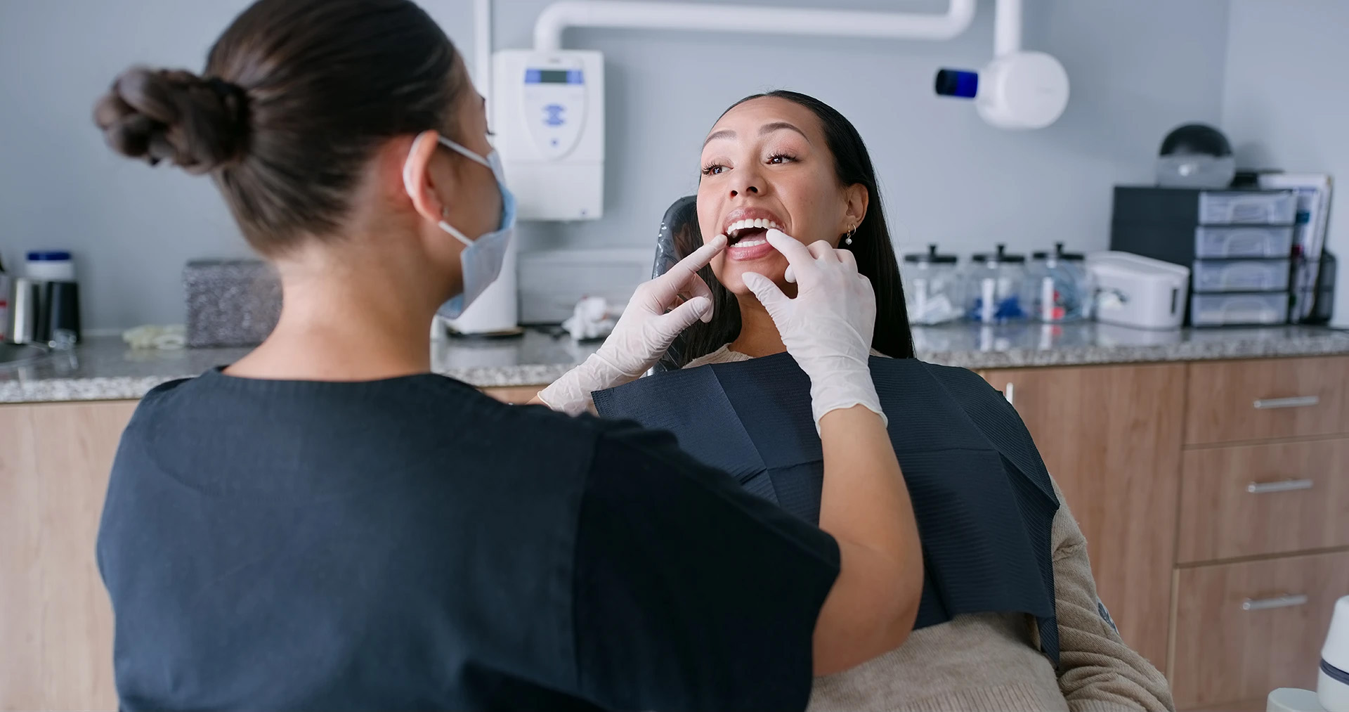 Masked dental professional pointing at a smiling woman's teeth during an examination