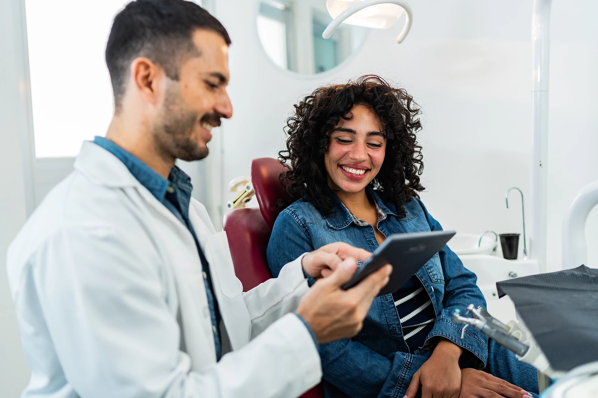 Smiling dentist showing a tablet to a happy woman patient in the dental chair