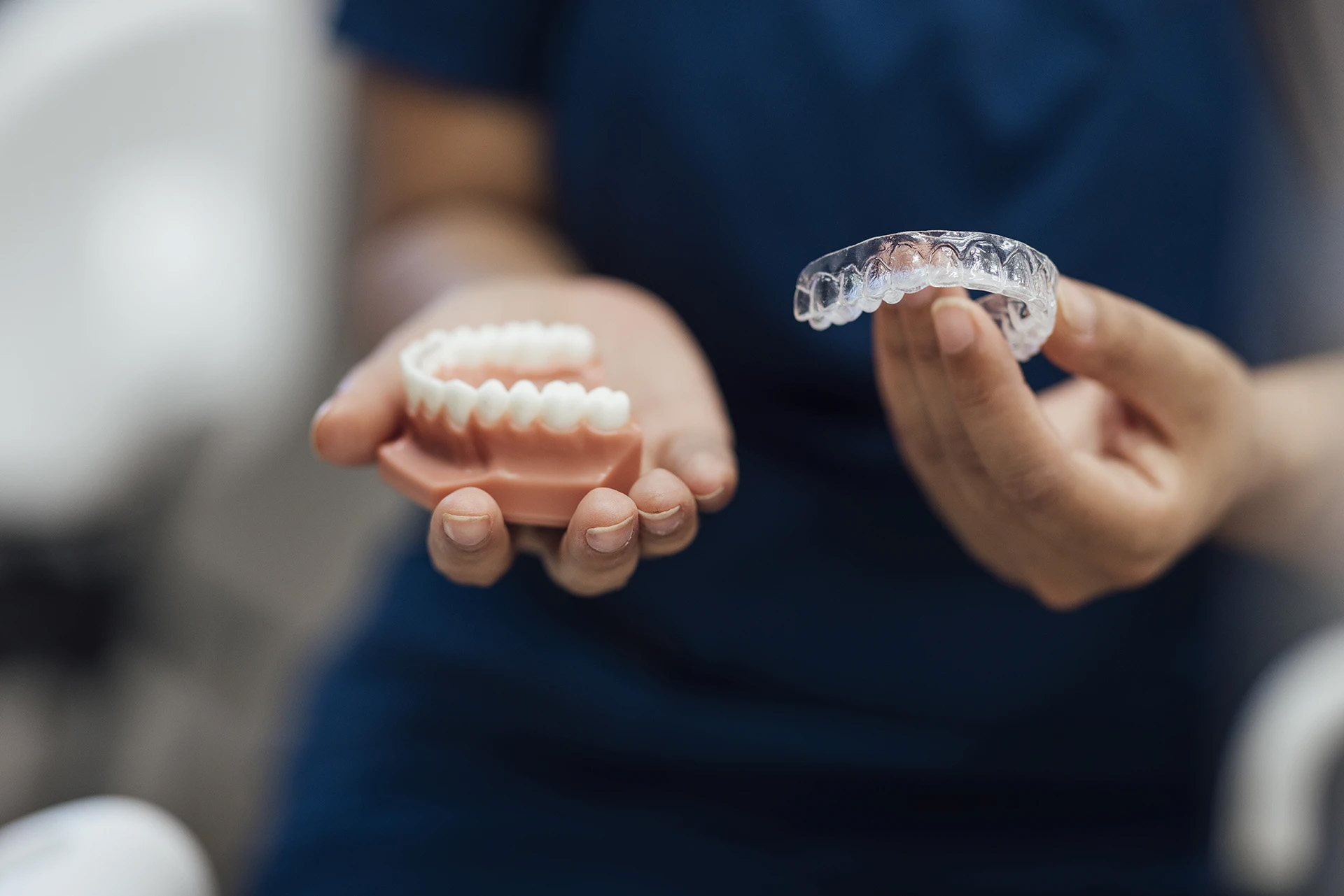 Dental professional holding a full denture in one hand and a clear aligner in the other
