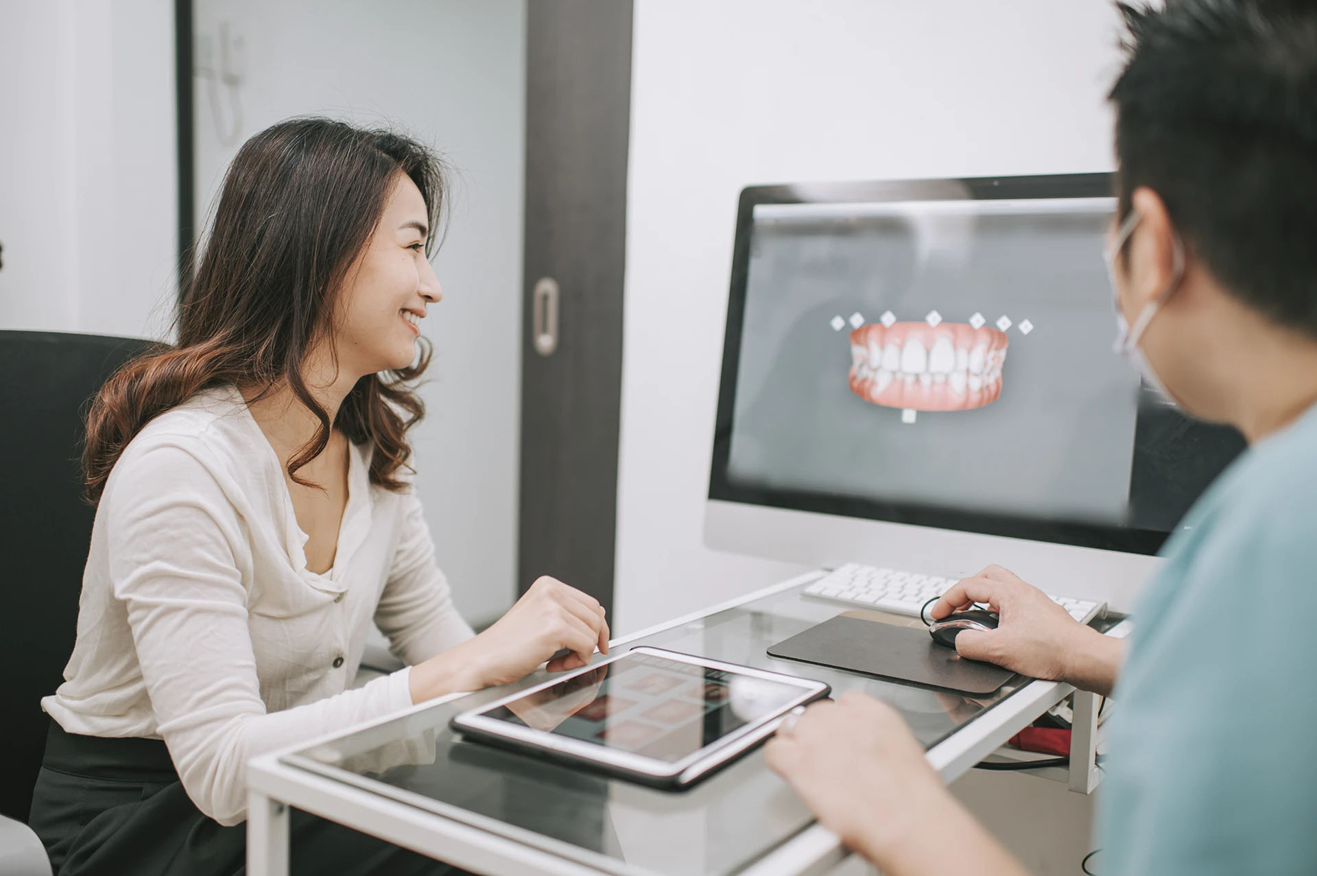 Smiling woman at a consultation as a dentist shows a 3D model of teeth on a computer screen