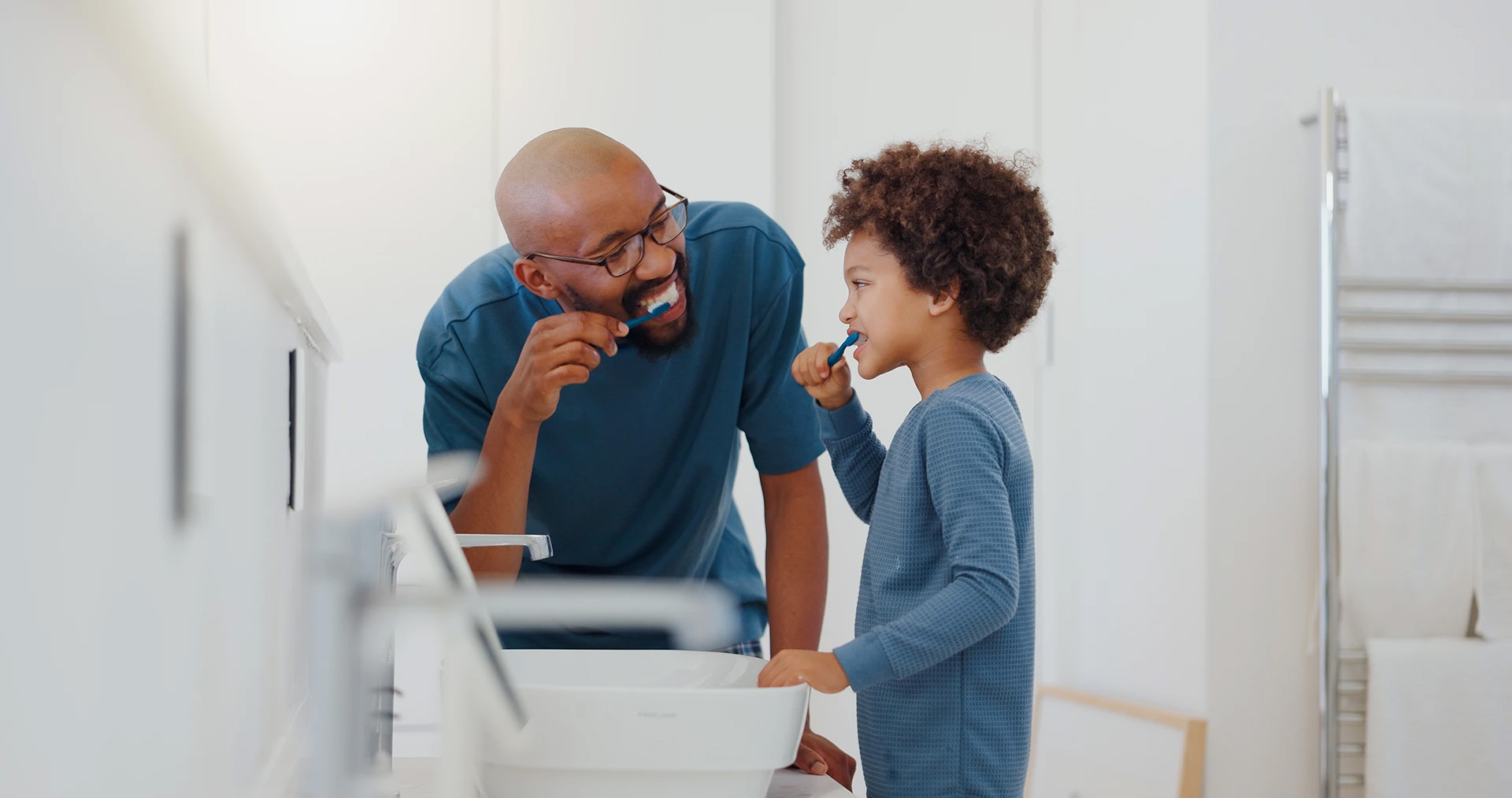 Smiling father and his young son brushing their teeth together at the bathroom sink