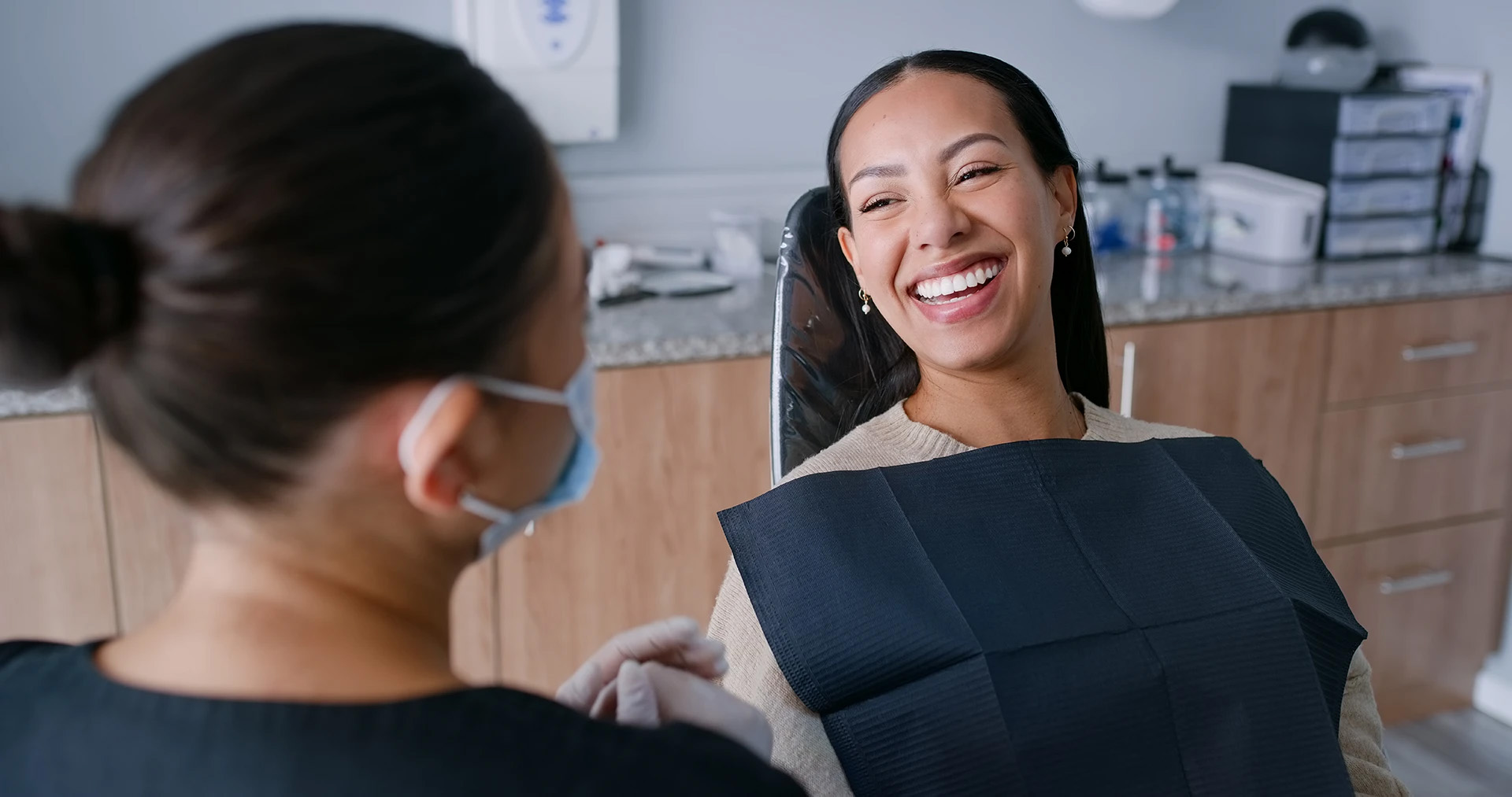 Smiling woman laughing in a dental chair while a masked dental professional chats with her