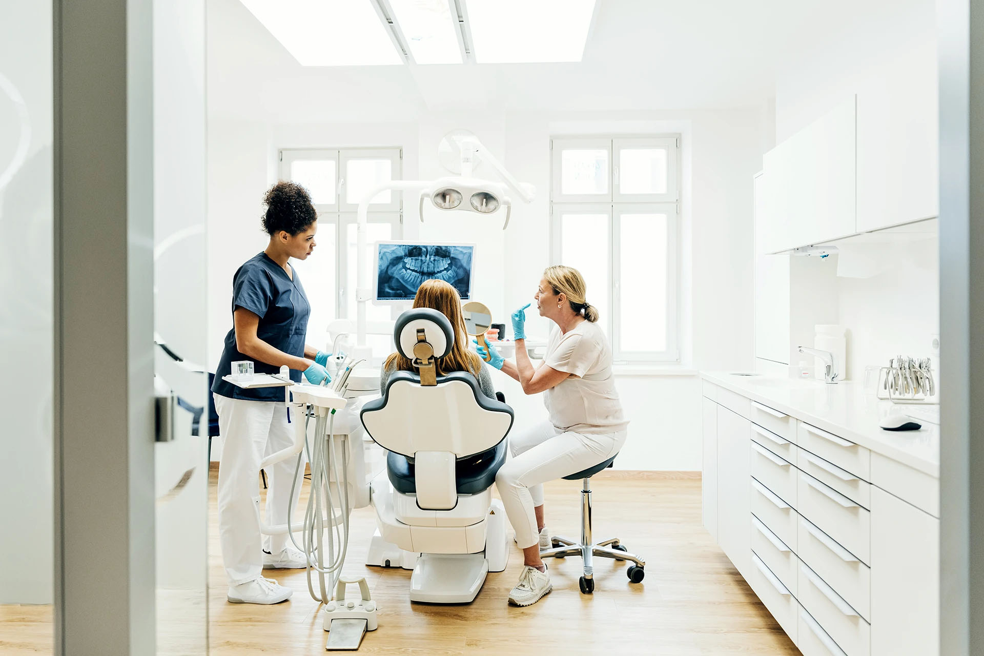 Bright modern dental operatory with an assistant, a reclined patient and a dentist during an appointment