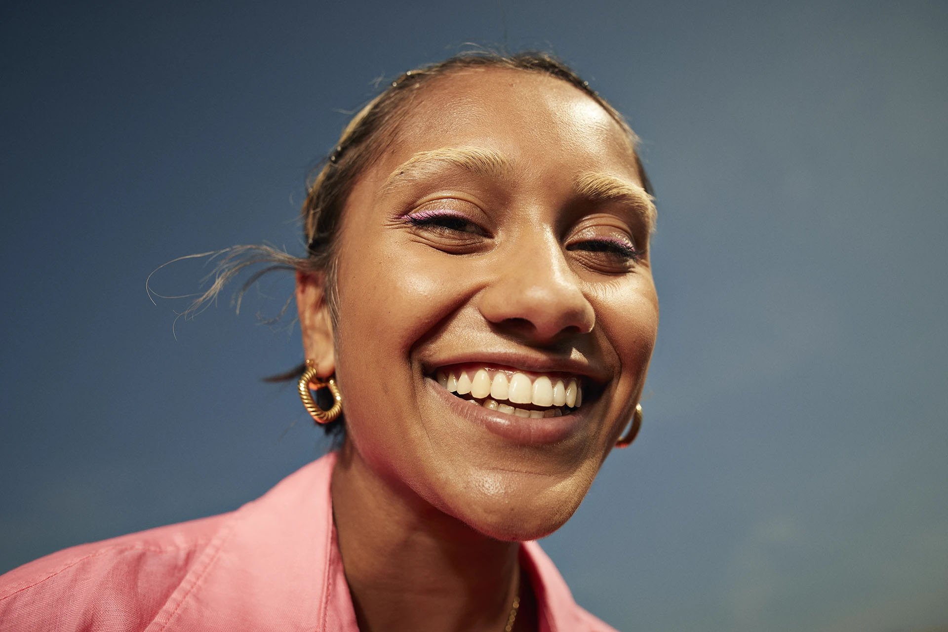 Studio portrait of a smiling woman in a pink shirt with a bright smile against a blue background