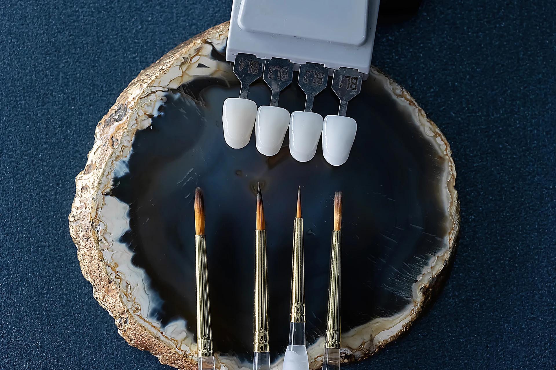Flat lay of bleach-shade veneer samples and fine ceramic brushes on an agate slice