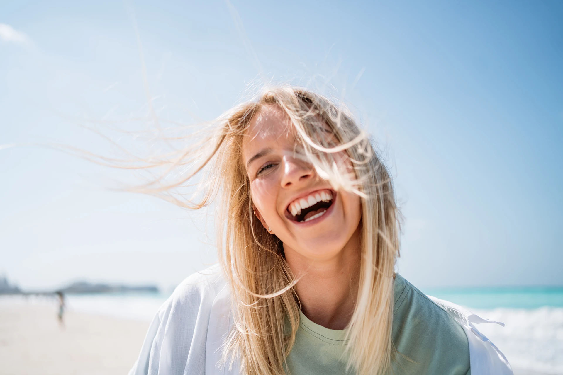 Blonde woman laughing joyfully on a sunny beach with the sea behind her