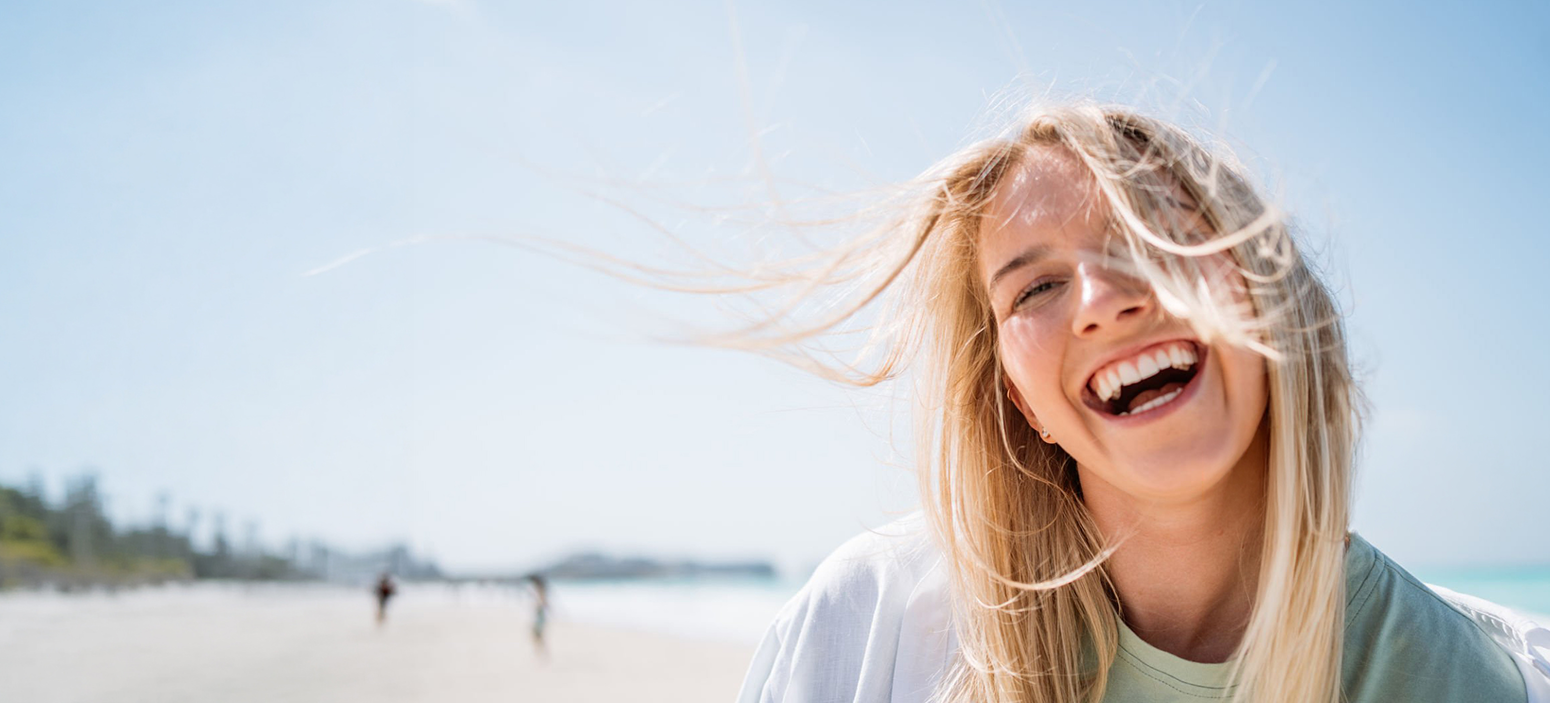 Blonde woman laughing joyfully on a sunny beach with the sea behind her
